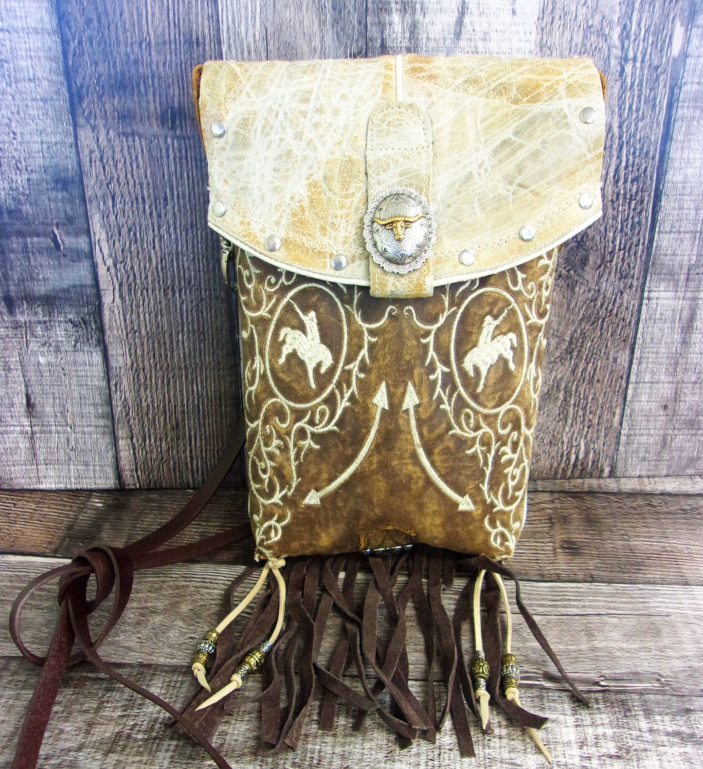 Leather bag with fringe and embossed designs on a wooden surface