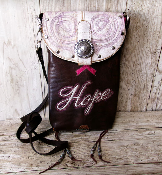 Brown leather bag with embroidered 'Hope' on a wooden surface
