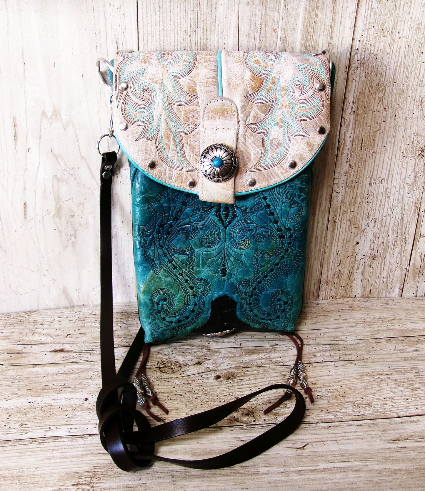 Leather handbag with turquoise design and white decorative flap on a wooden surface