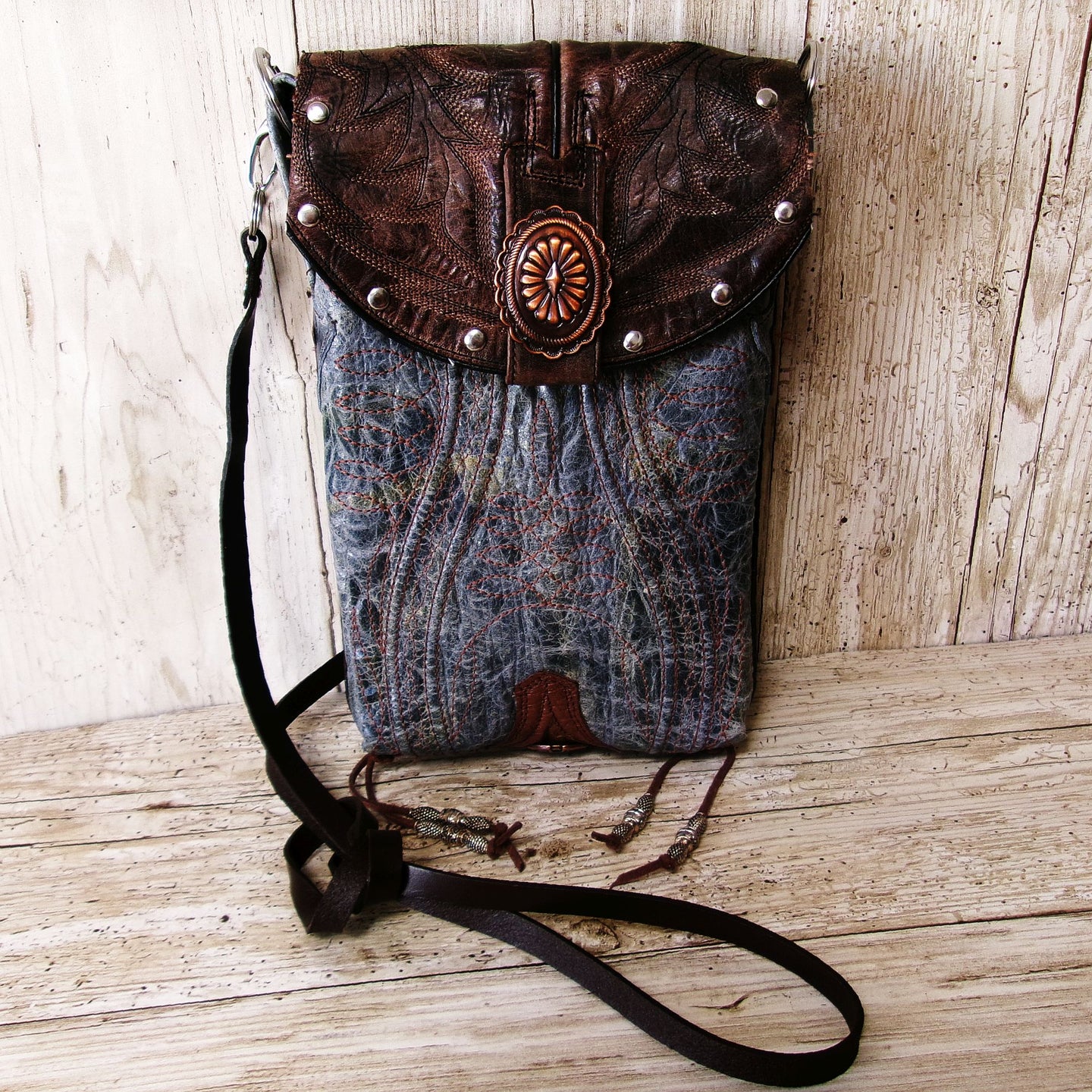 Brown leather and denim handbag with decorative elements on a wooden surface
