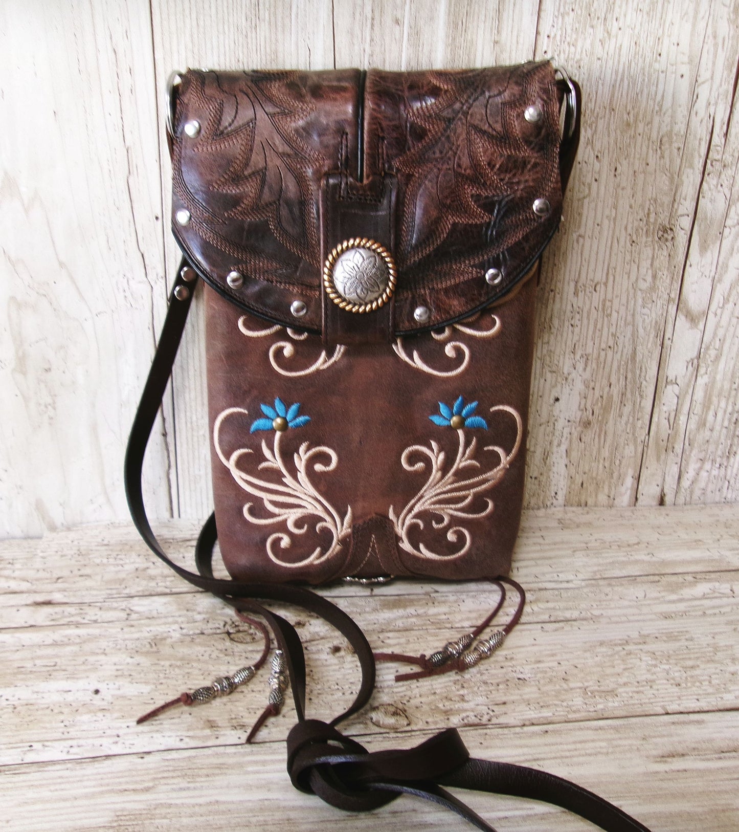 Brown leather bag with floral embroidery and decorative elements on a wooden surface