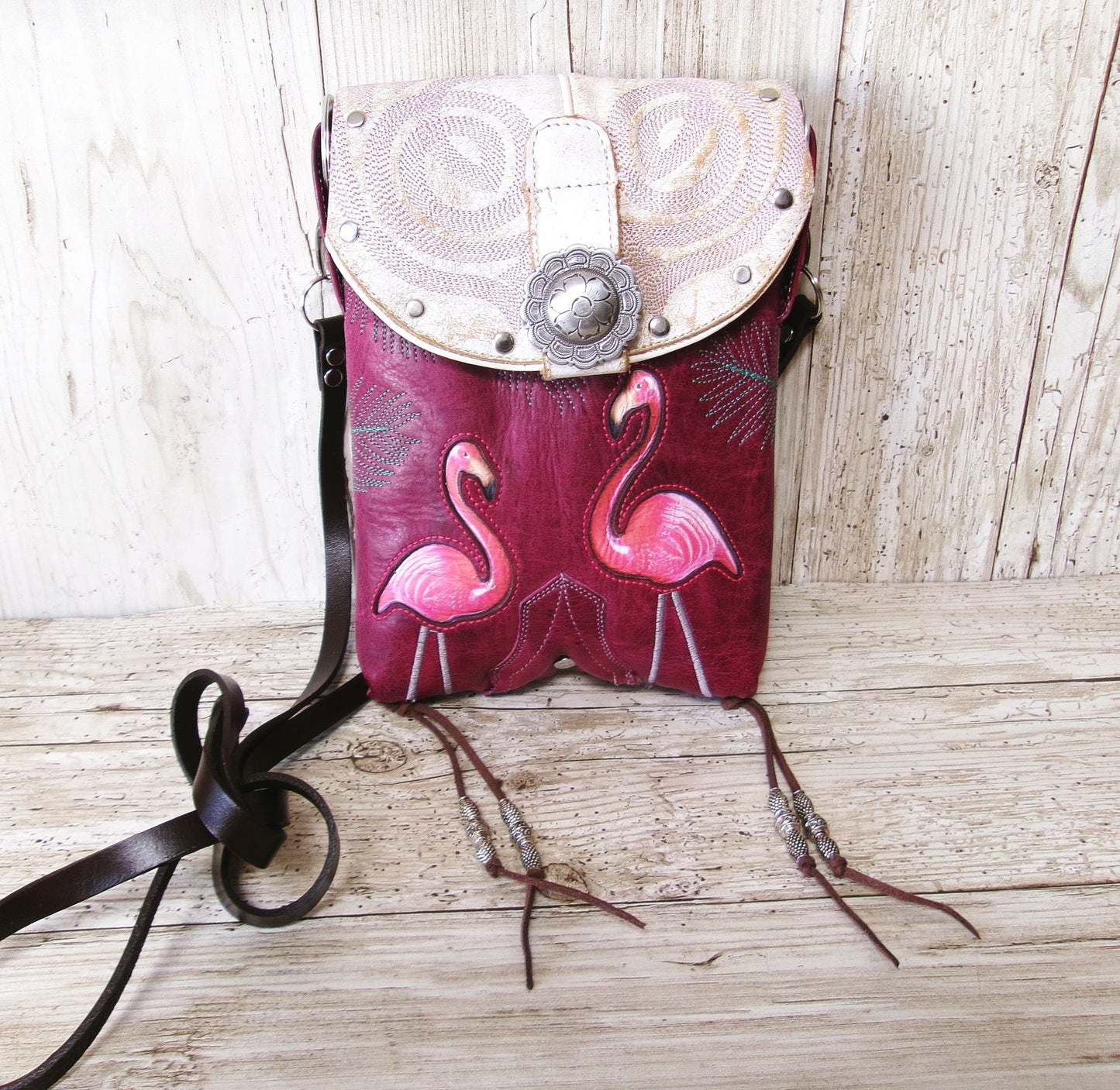 Pink leather bag with flamingo design and white flap on a wooden surface