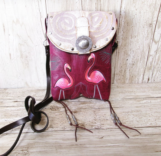 Pink leather bag with flamingo design and white flap on a wooden surface