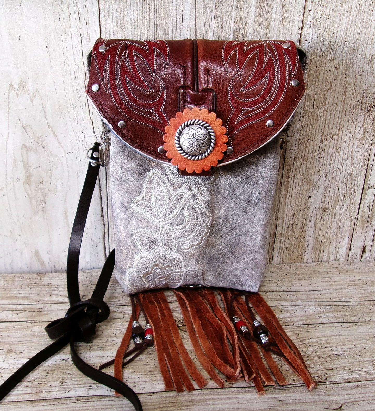 Leather handbag with floral embroidery and fringe on a wooden surface