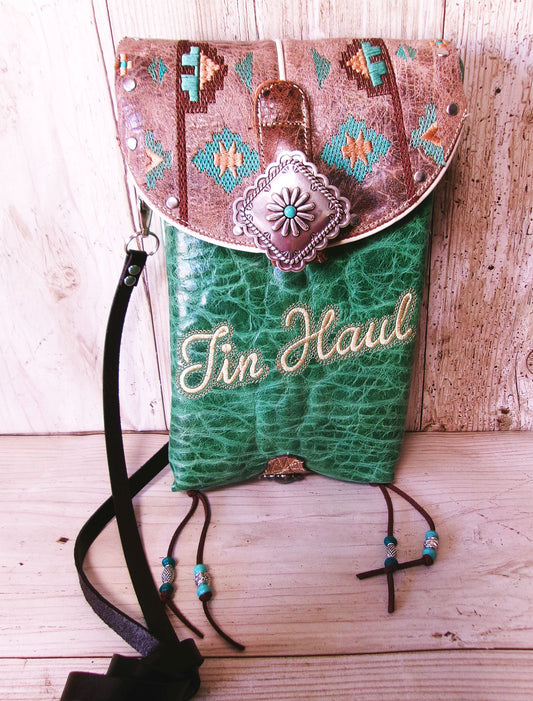 Green leather bag with decorative brown top section on a wooden surface