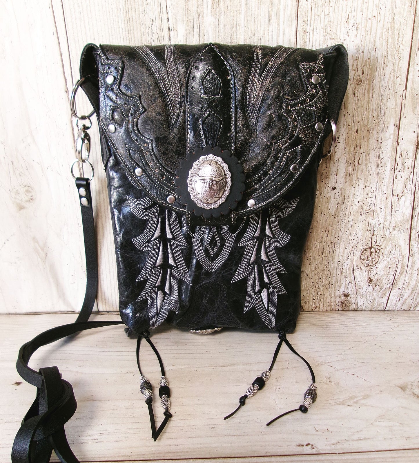 Black leather handbag with intricate silver embroidery on a wooden surface