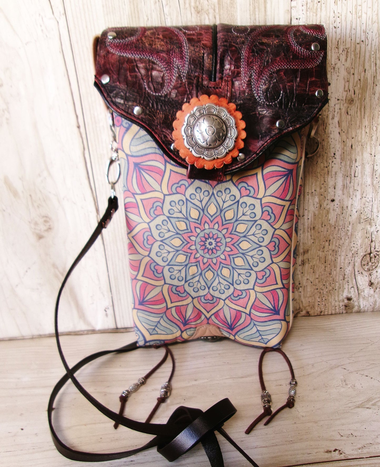 Multicolored patterned bag with leather flap and decorative element on a wooden surface