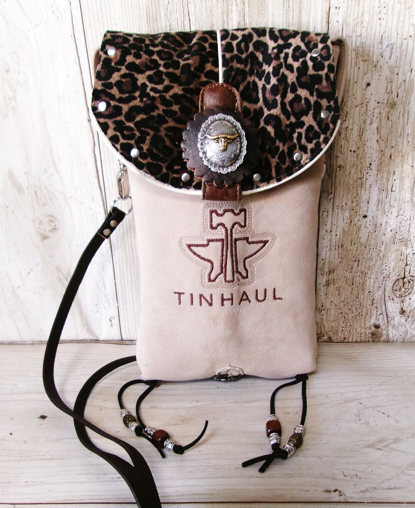 Leopard print top flap bag with 'Tin haul' branding on a wooden surface