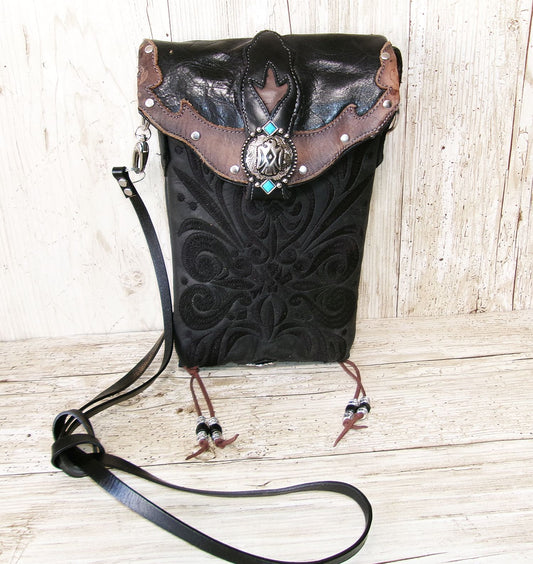 Black leather handbag with intricate patterns and decorative elements on a wooden surface