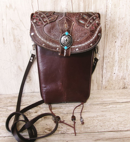 Brown leather bag with intricate designs and a decorative clasp on a wooden surface