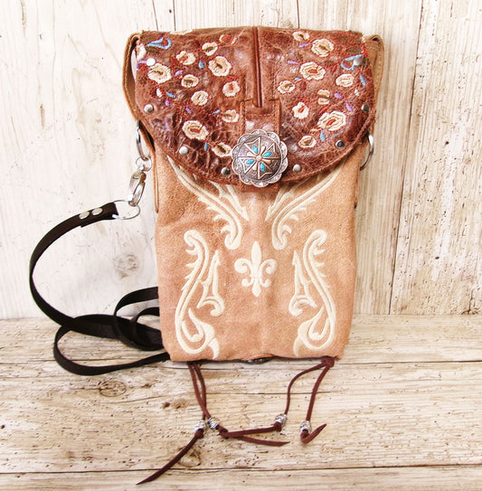Brown leather handbag with floral embroidery and decorative clasp on a wooden surface