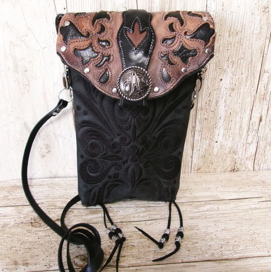 Black leather bag with intricate brown tooled design on a wooden surface