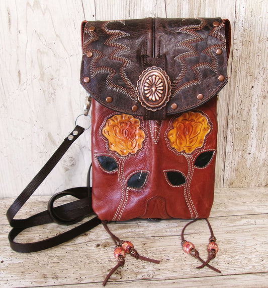Brown leather bag with floral designs and decorative elements on a wooden surface