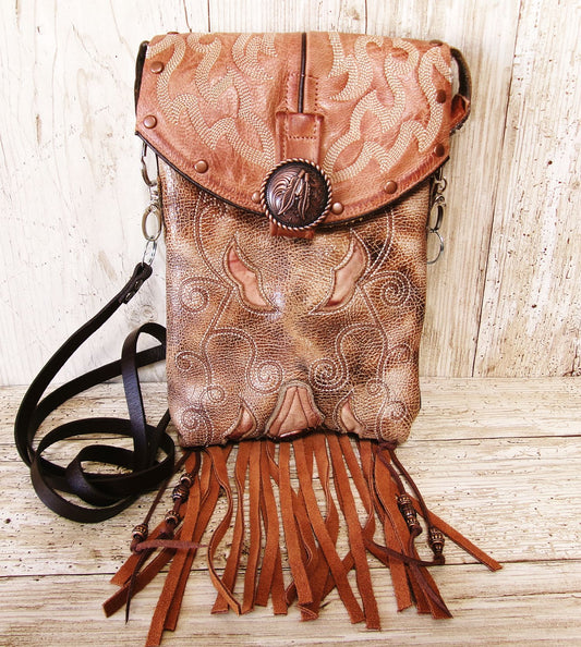 Brown leather bag with intricate patterns and fringes on a wooden surface