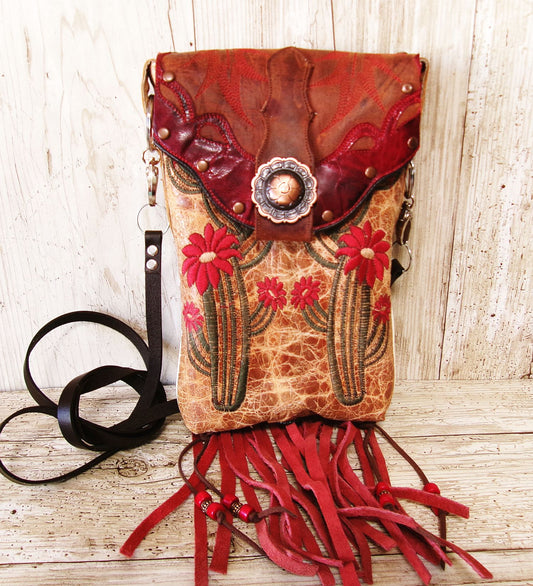 Handmade leather bag with floral embroidery and red fringe on a wooden surface