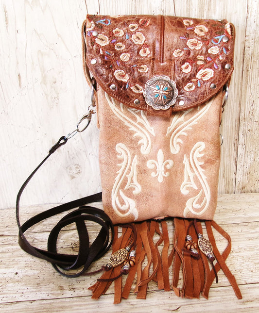 Brown leather handbag with floral embroidery and fringe on a wooden surface