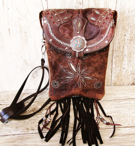 Brown leather bag with intricate designs and fringes on a wooden surface
