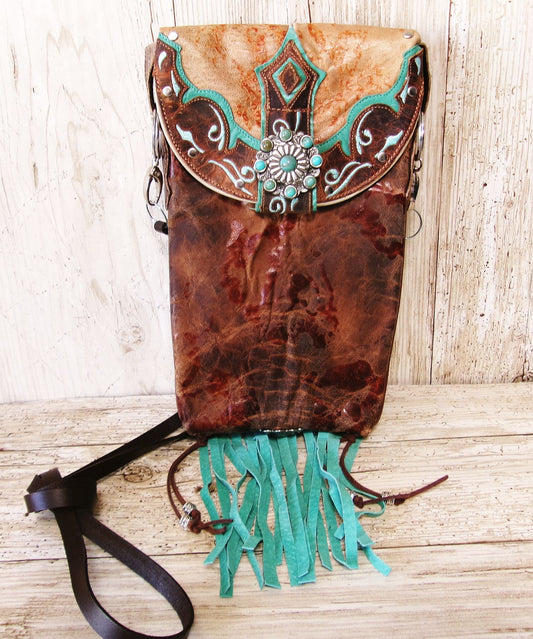 Brown leather bag with turquoise fringe and decorative elements on a wooden surface