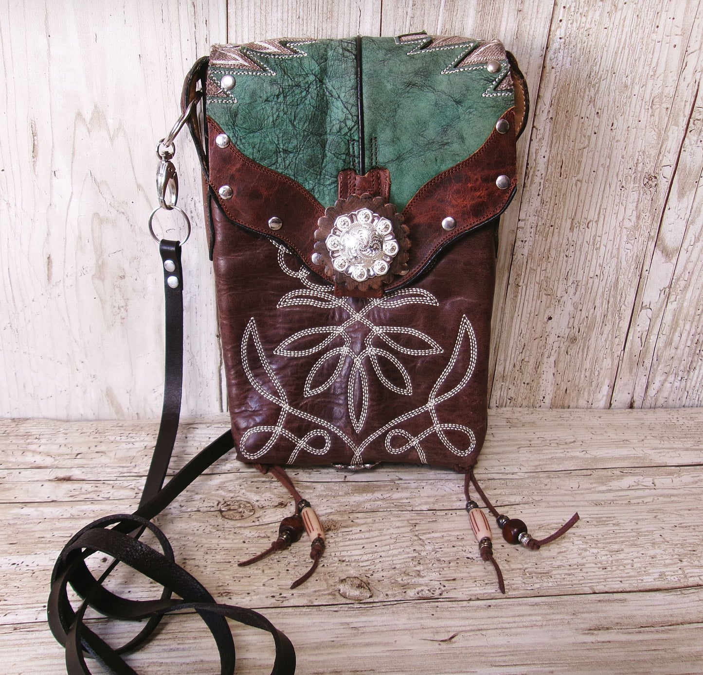 Brown leather crossbody bag with decorative elements on a wooden surface