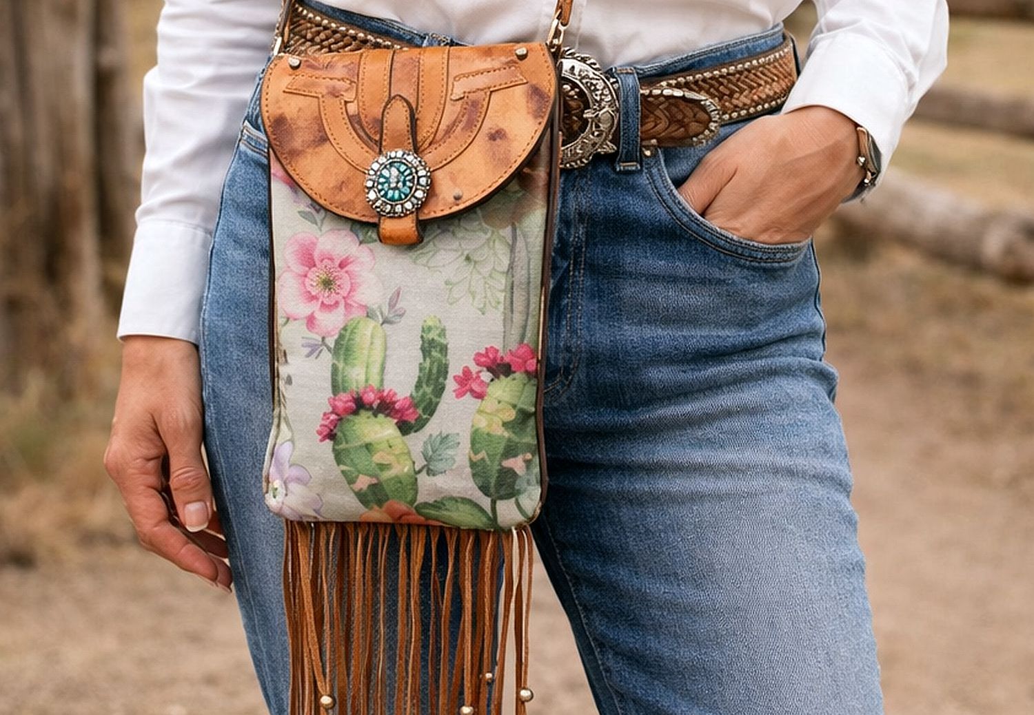 Person wearing a floral and cactus-patterned handbag with fringe, held in front of jeans.