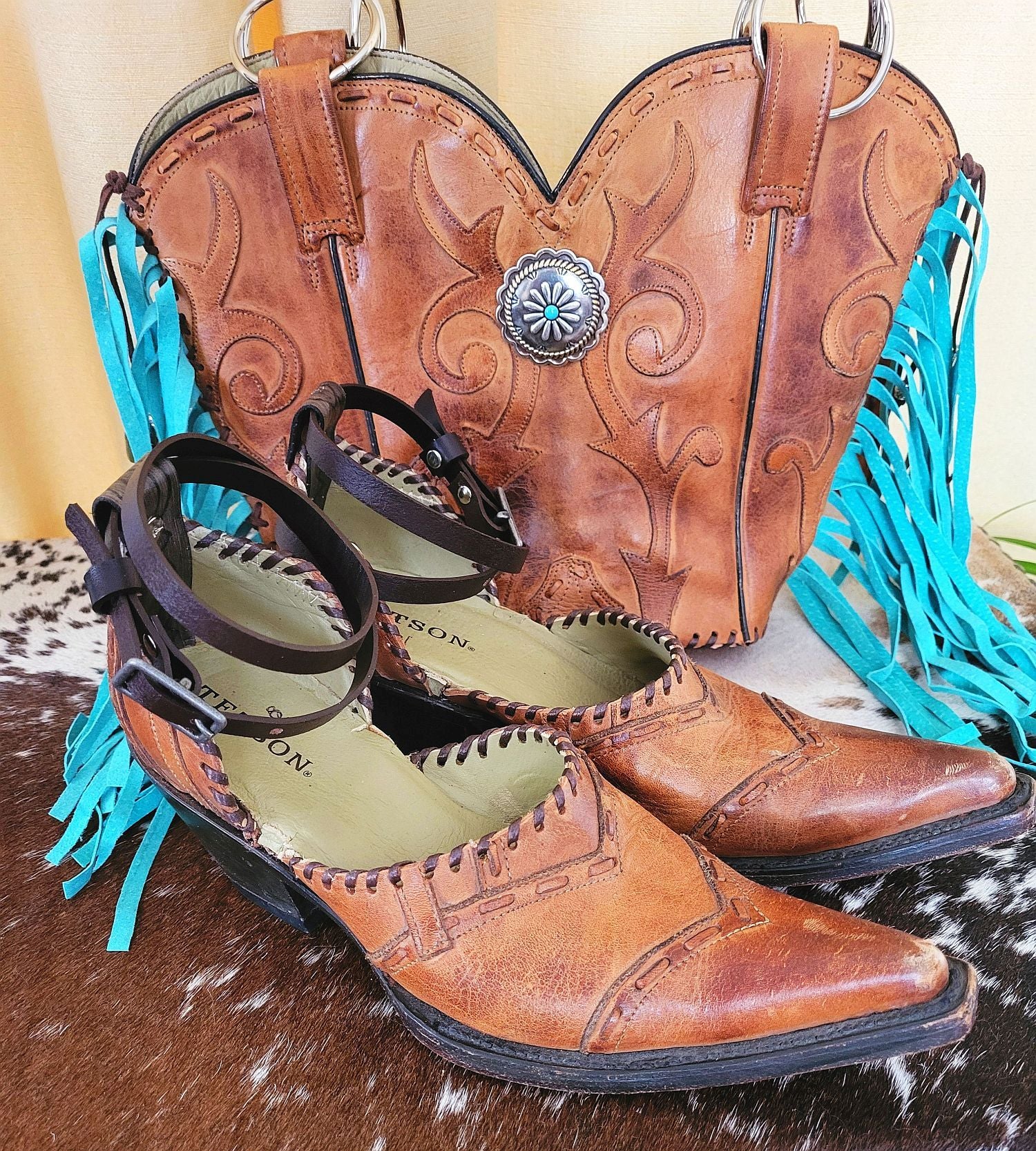 Pair of brown cowboy boots with turquoise fringes on a wooden surface.