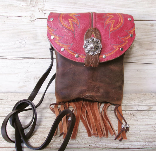 Brown leather handbag with pink top section and decorative elements on a wooden surface