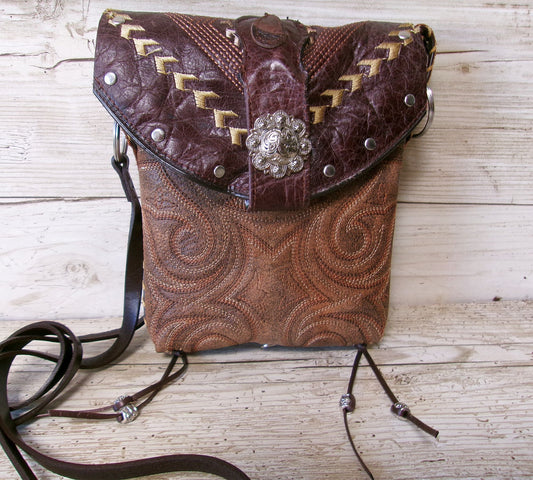 Brown leather handbag with intricate patterns and a decorative brooch on a wooden surface