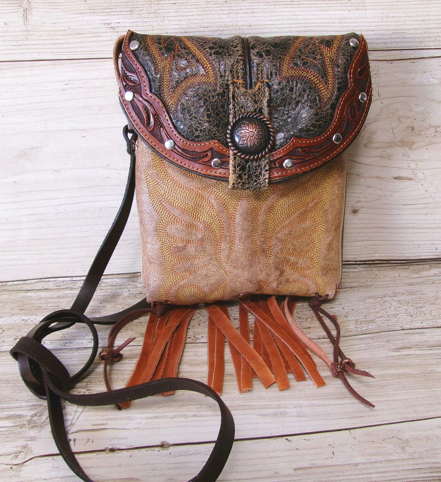 Brown leather crossbody bag with intricate patterns and fringes on a wooden surface