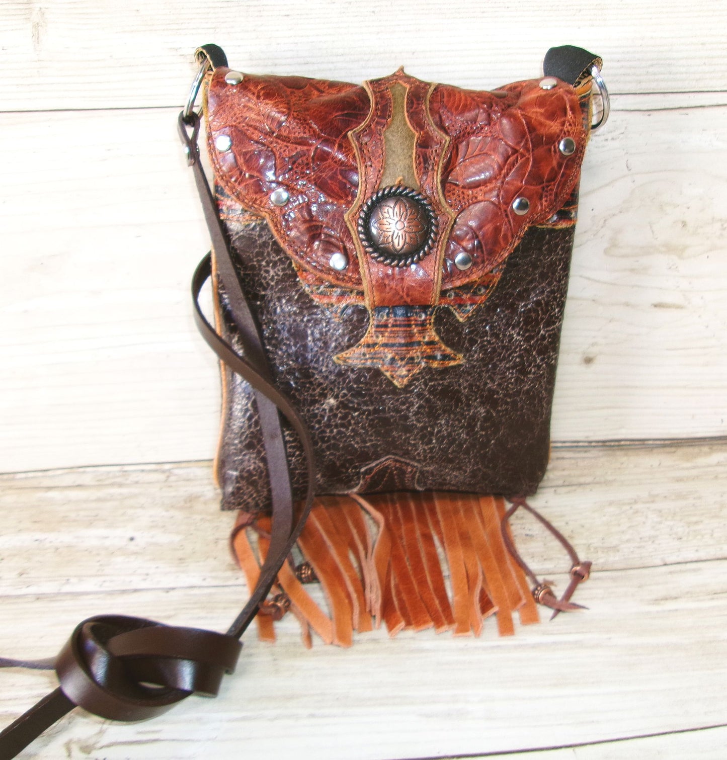 Brown leather handbag with intricate designs and fringes on a wooden surface