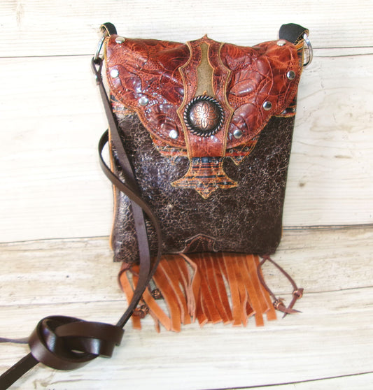 Brown leather handbag with intricate designs and fringes on a wooden surface