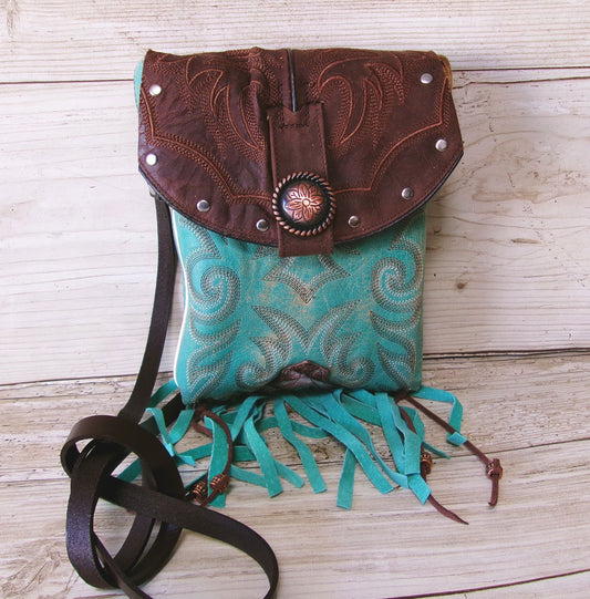 Turquoise and brown leather bag with fringe on a wooden surface