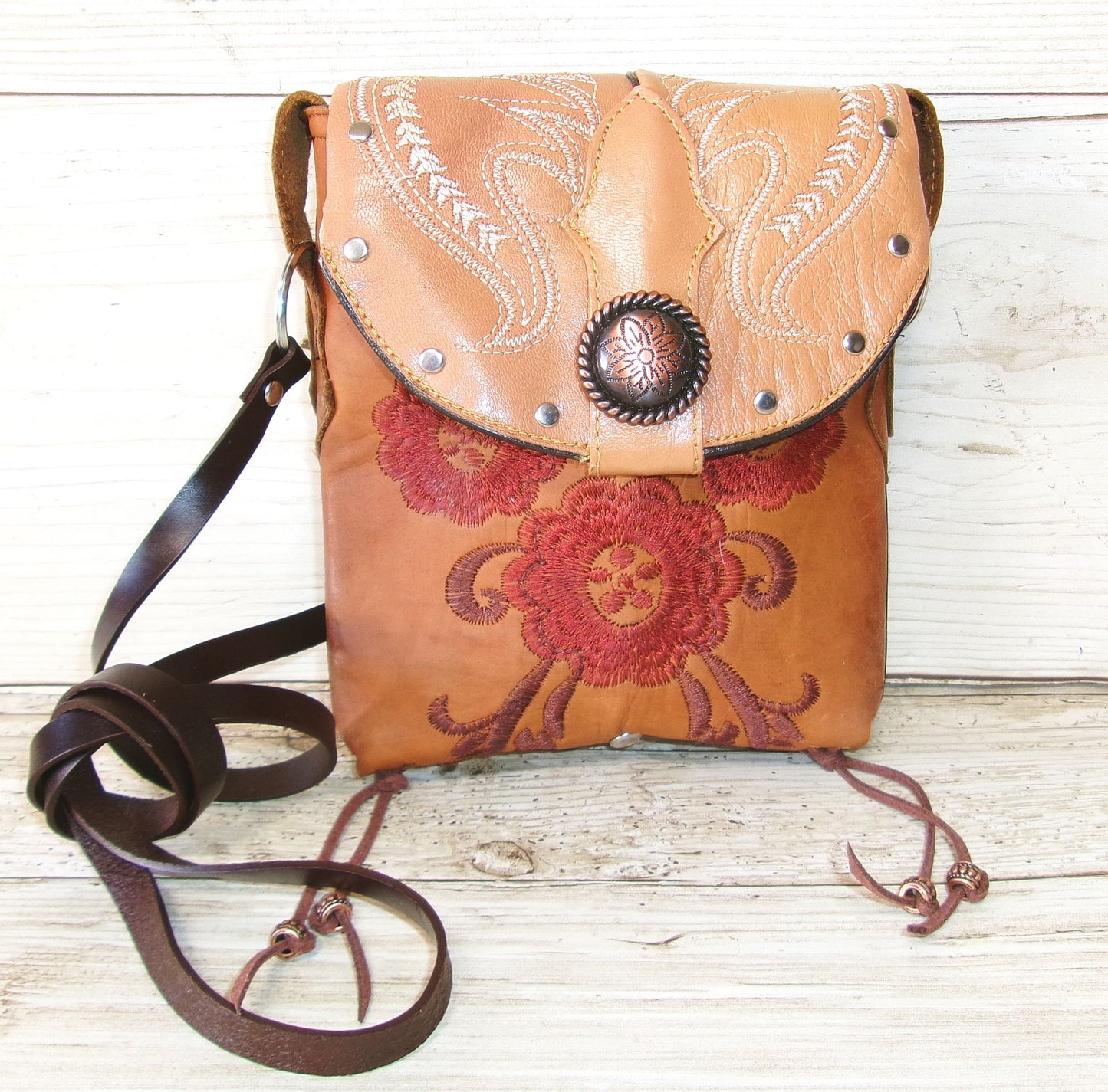 Brown leather crossbody bag with floral embroidery on a wooden surface