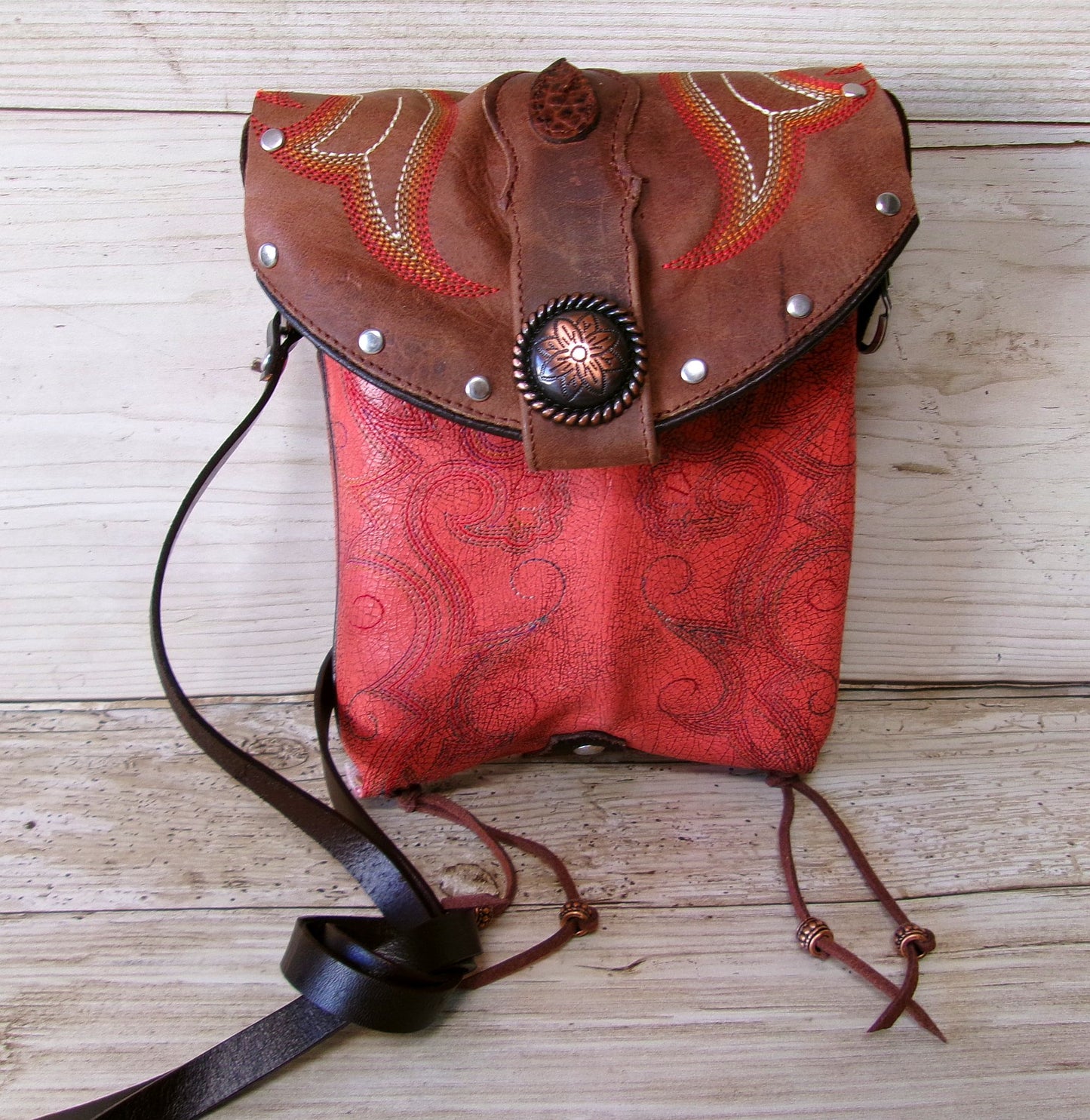 Red and brown leather bag with decorative elements on a wooden surface