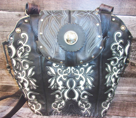 Black leather handbag with white embroidery and gold accents on a wooden surface