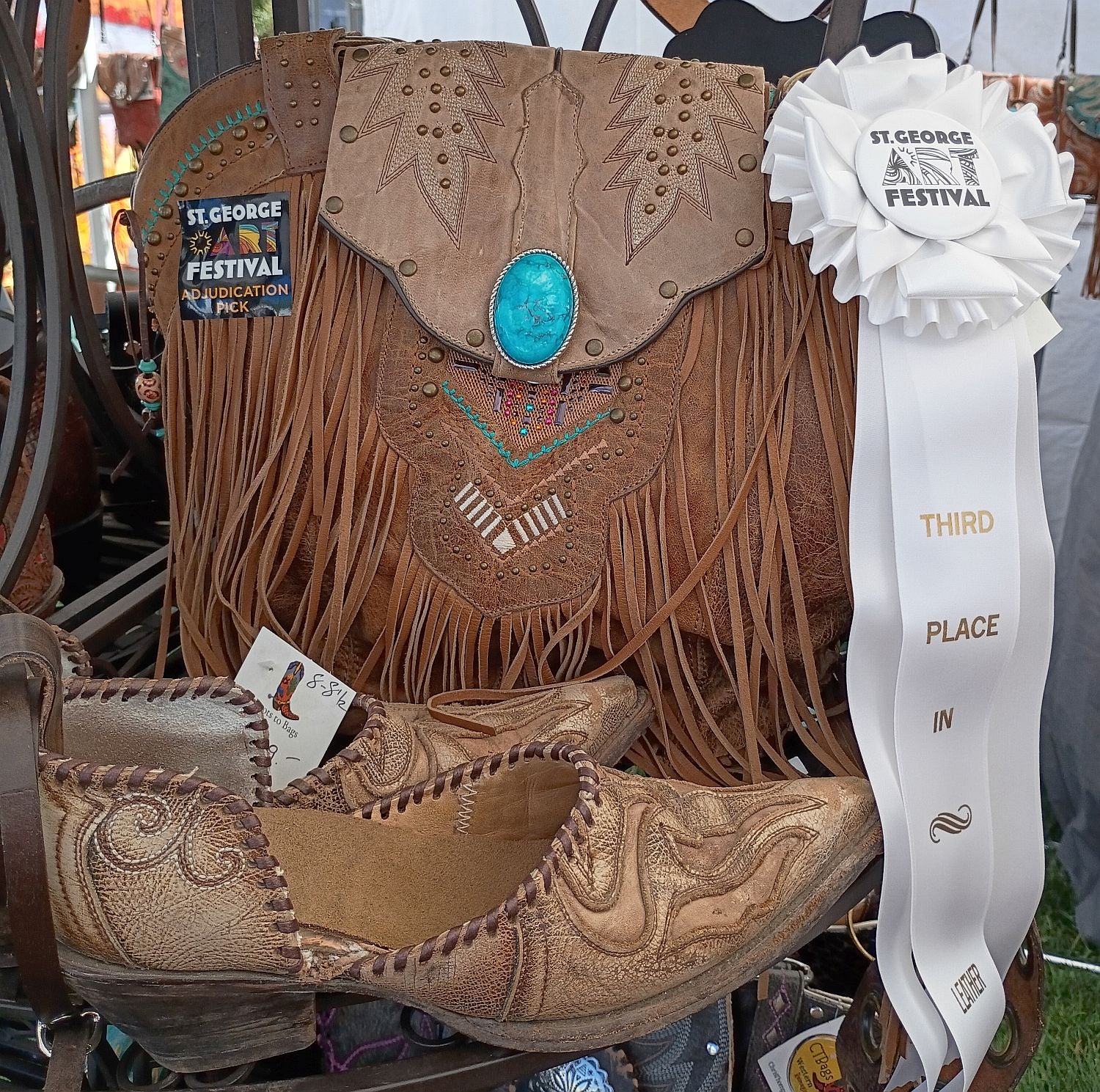 Brown leather boot with fringes and decorative elements, featuring a ribbon indicating 'Third Place' at the St. George Art Festival.