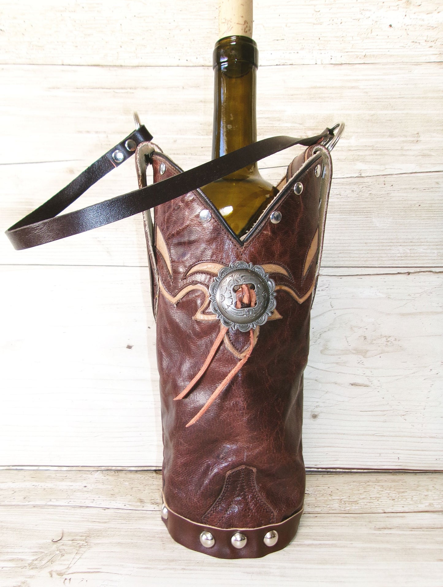 Wine bottle in a brown leather boot with decorative elements on a wooden surface