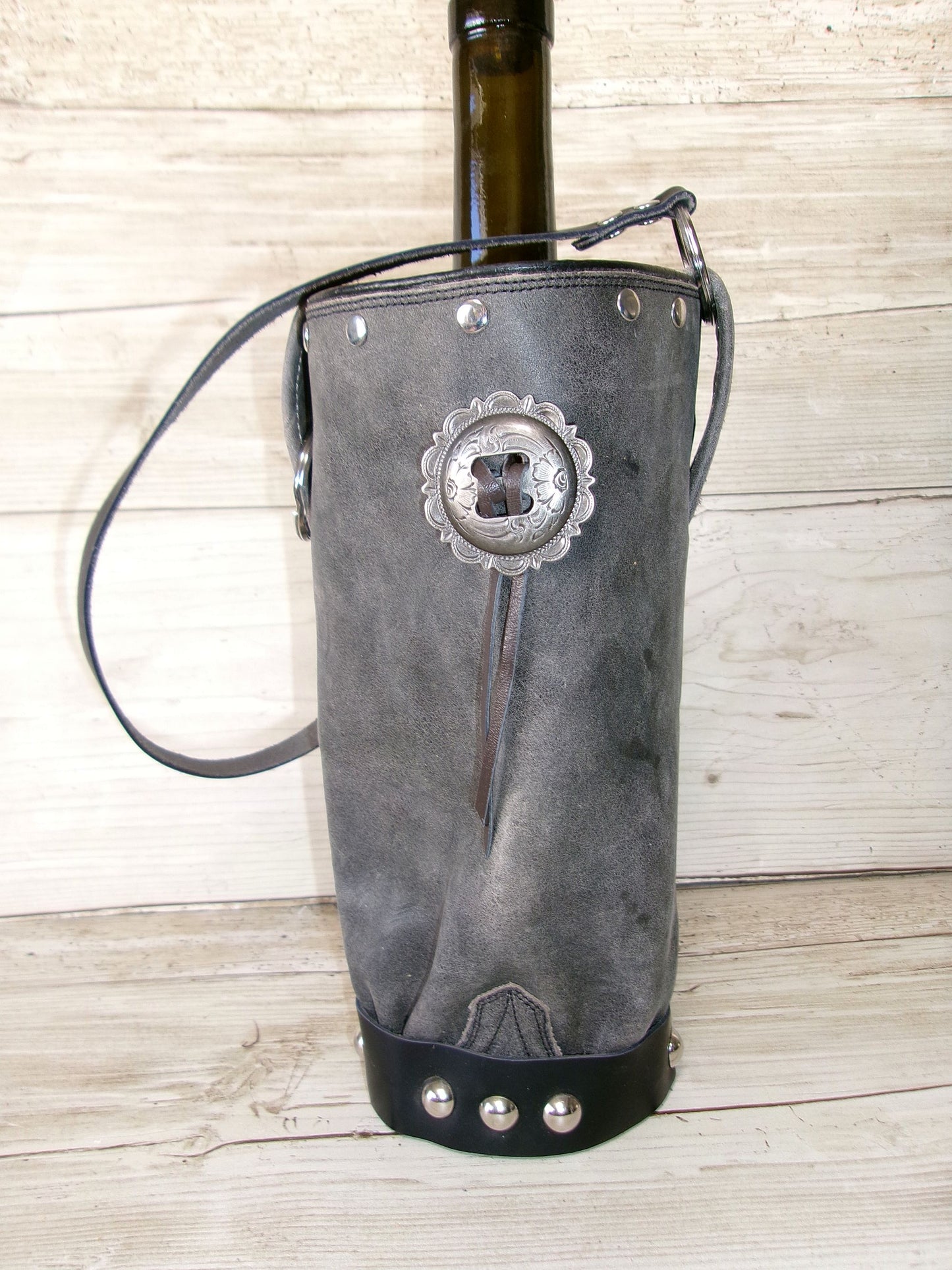 Gray leather wine holder with decorative concho on a wooden surface