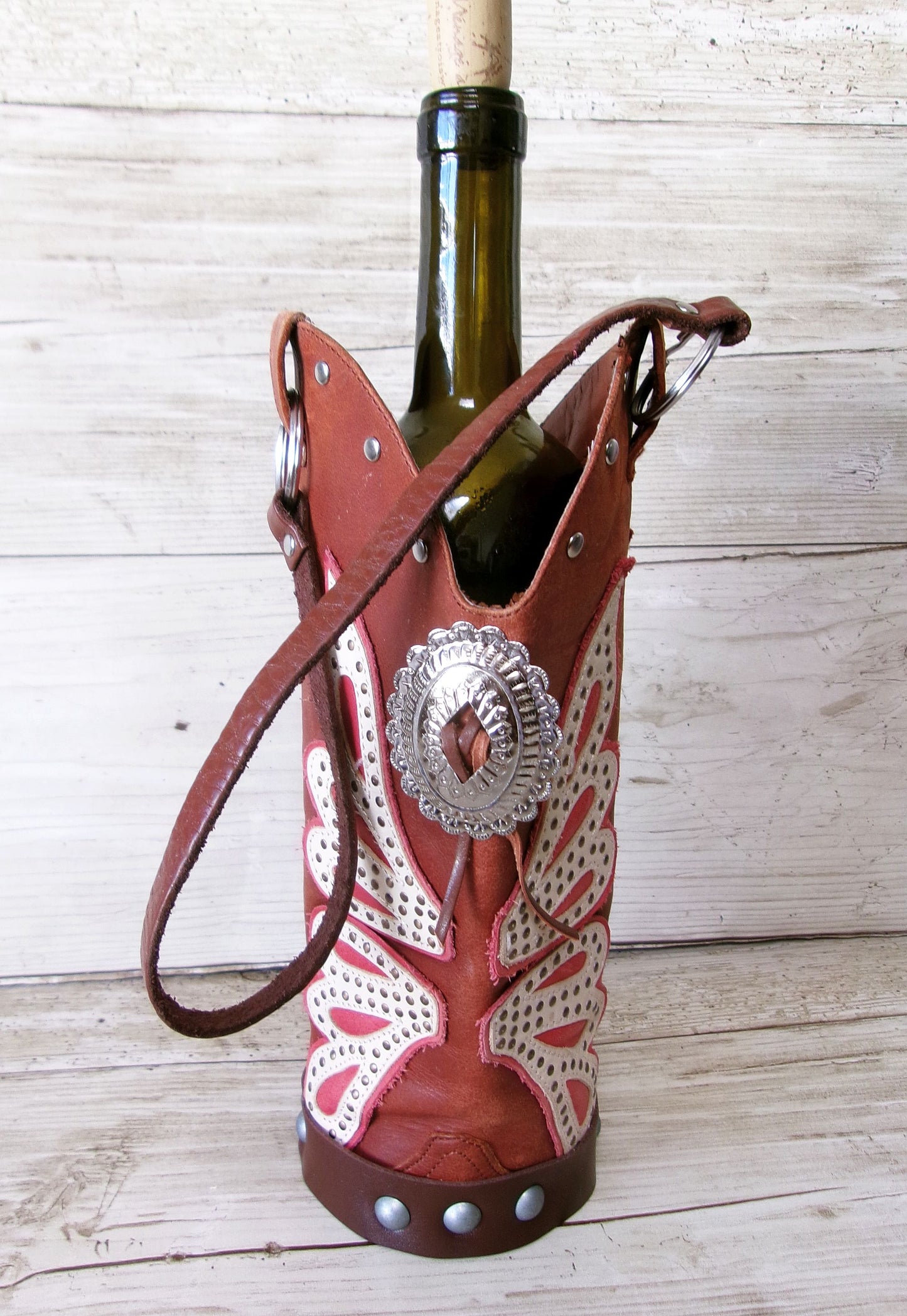 Wine bottle holder shaped like a cowboy boot with decorative elements on a wooden surface.