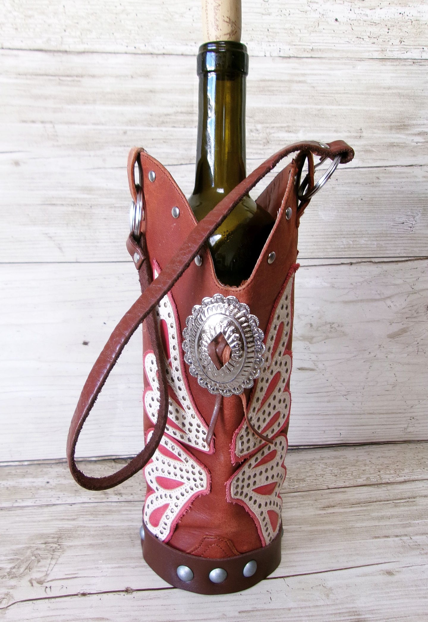 Wine bottle holder shaped like a cowboy boot with decorative elements on a wooden surface.