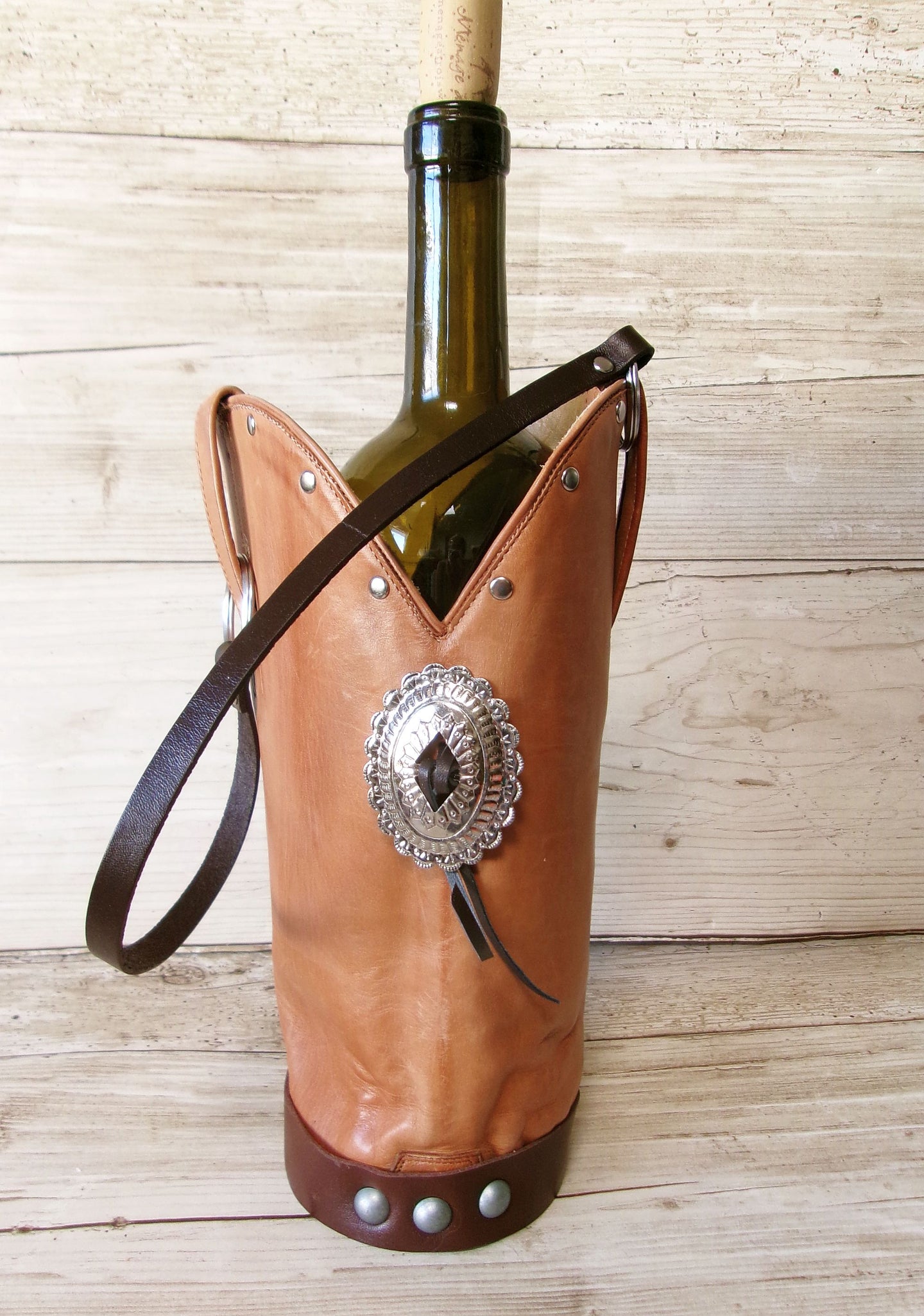 Wine bottle in a leather holder with decorative concho on a wooden surface