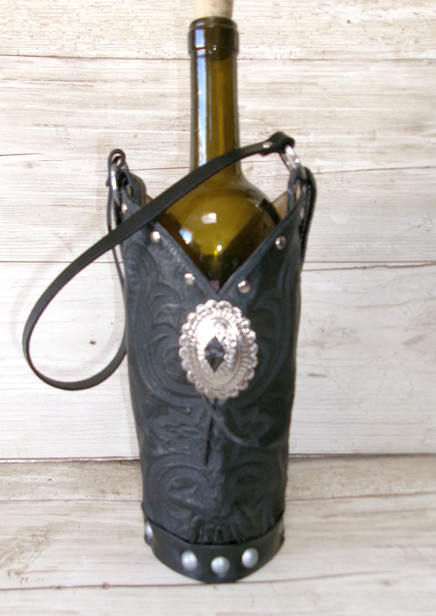 Wine bottle held in a black leather boot holder with silver concho on a wooden surface