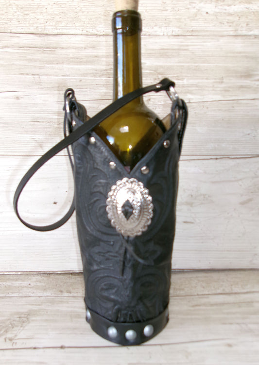Wine bottle held in a black leather boot holder with silver concho on a wooden surface