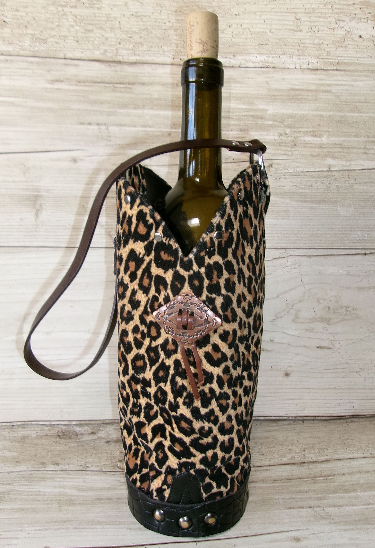 Wine bottle in a leopard print holder with a decorative emblem on a wooden surface