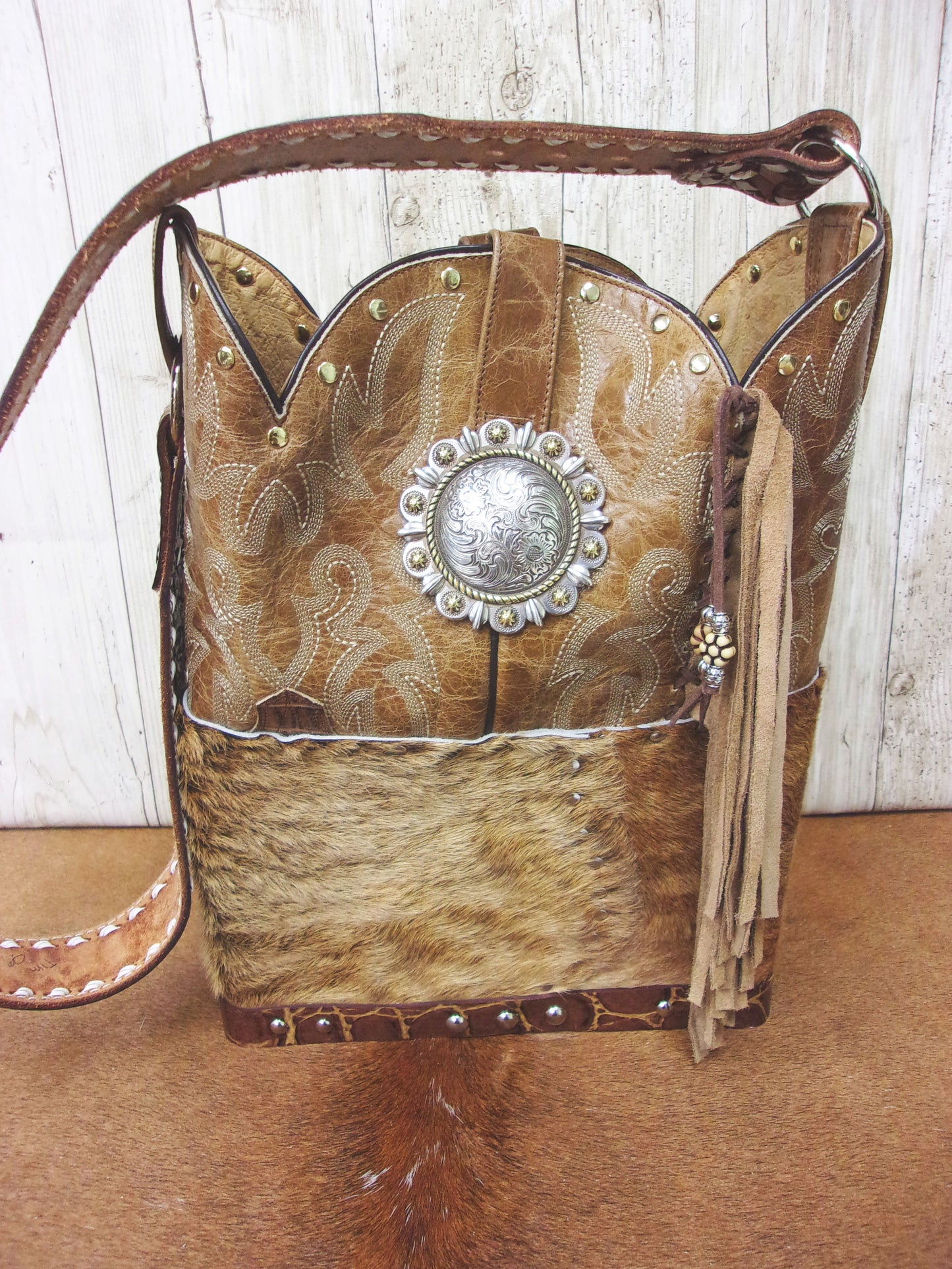 Cowboy-style handbag with leather accents and decorative concho on a wooden surface.