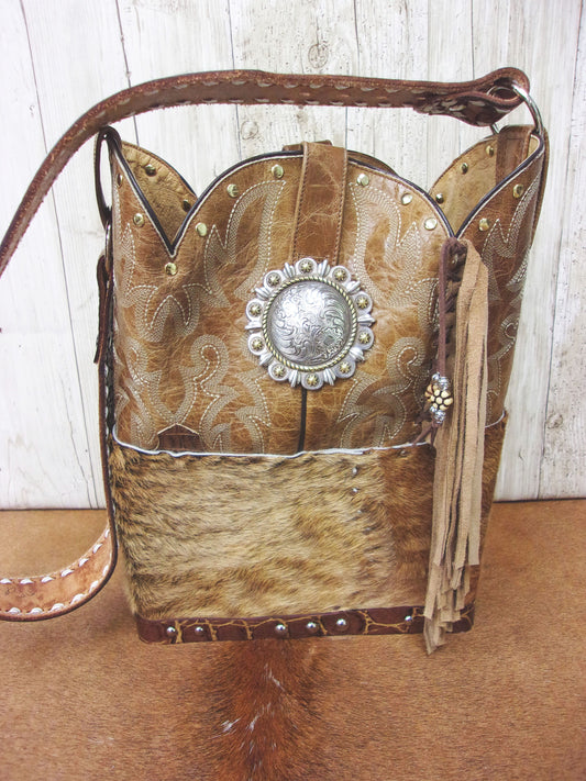 Cowboy-style handbag with leather accents and decorative concho on a wooden surface.