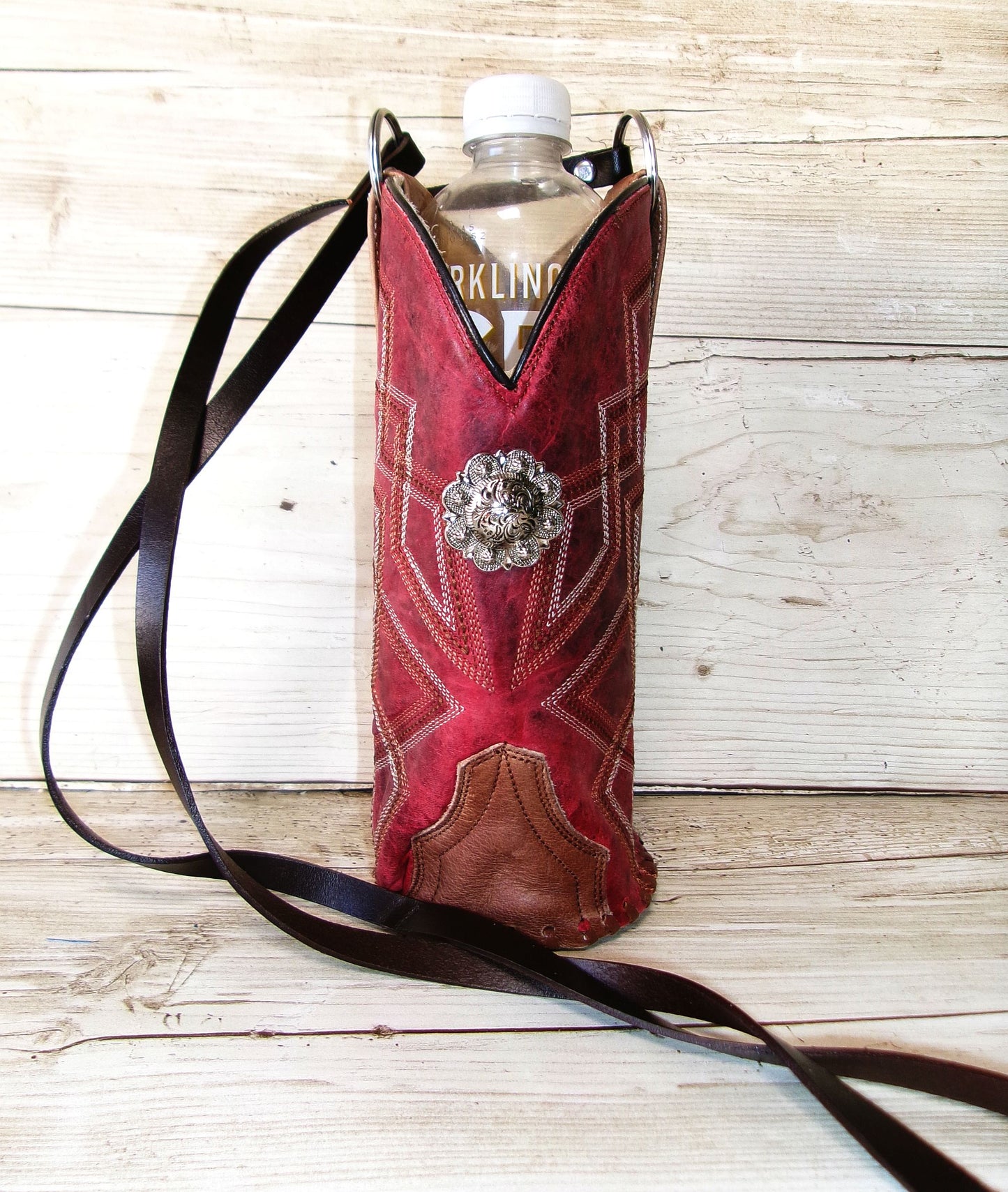 Red leather boot-shaped water bottle holder with decorative buckle on a wooden surface