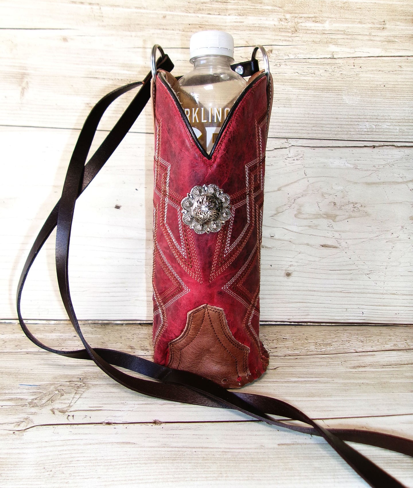 Red leather boot-shaped water bottle holder with decorative buckle on a wooden surface