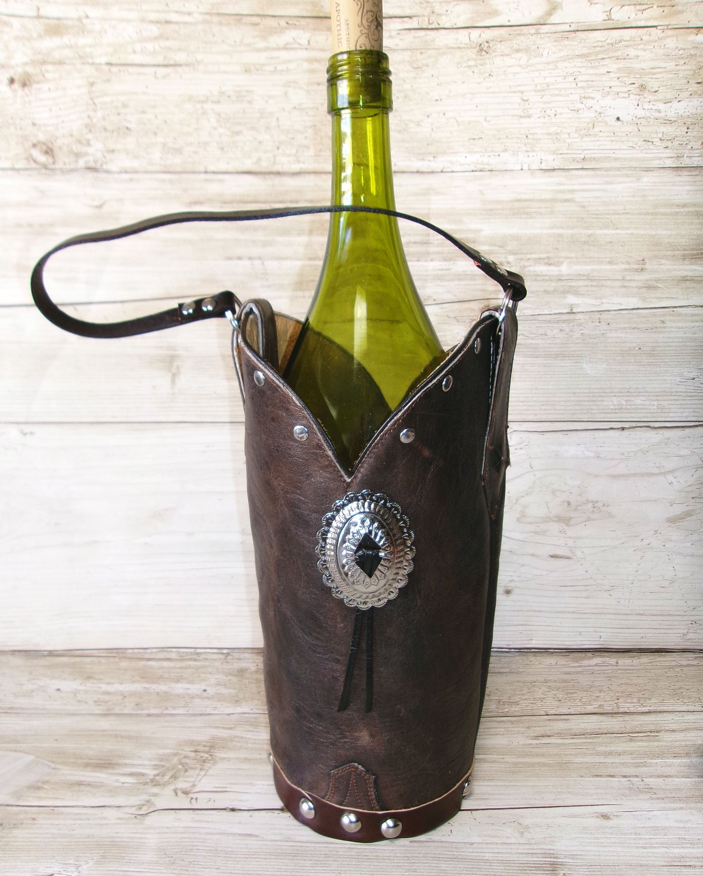 Brown leather wine bottle holder with decorative concho on a wooden surface