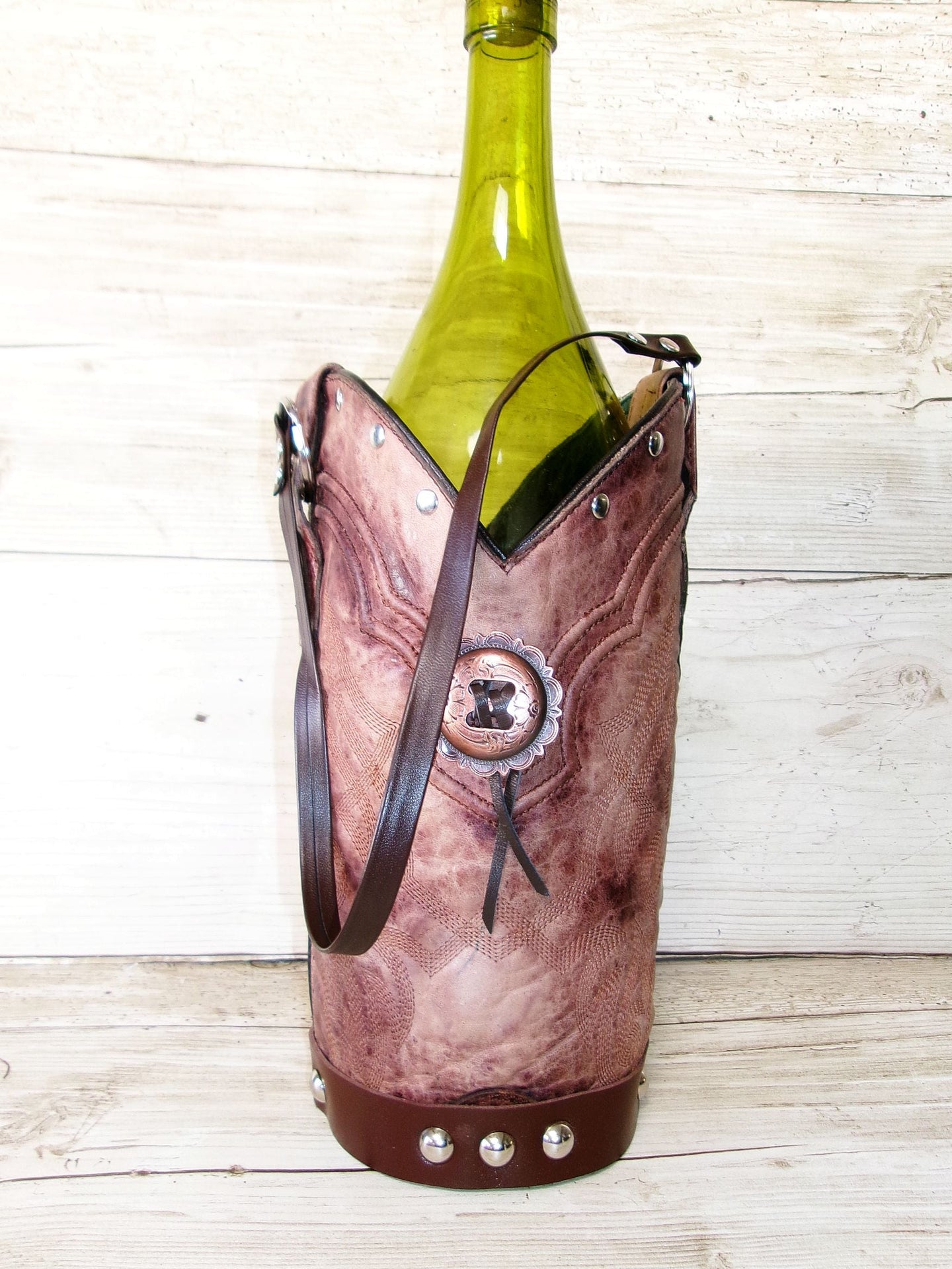 Brown leather wine bottle holder with a green wine bottle on a wooden surface