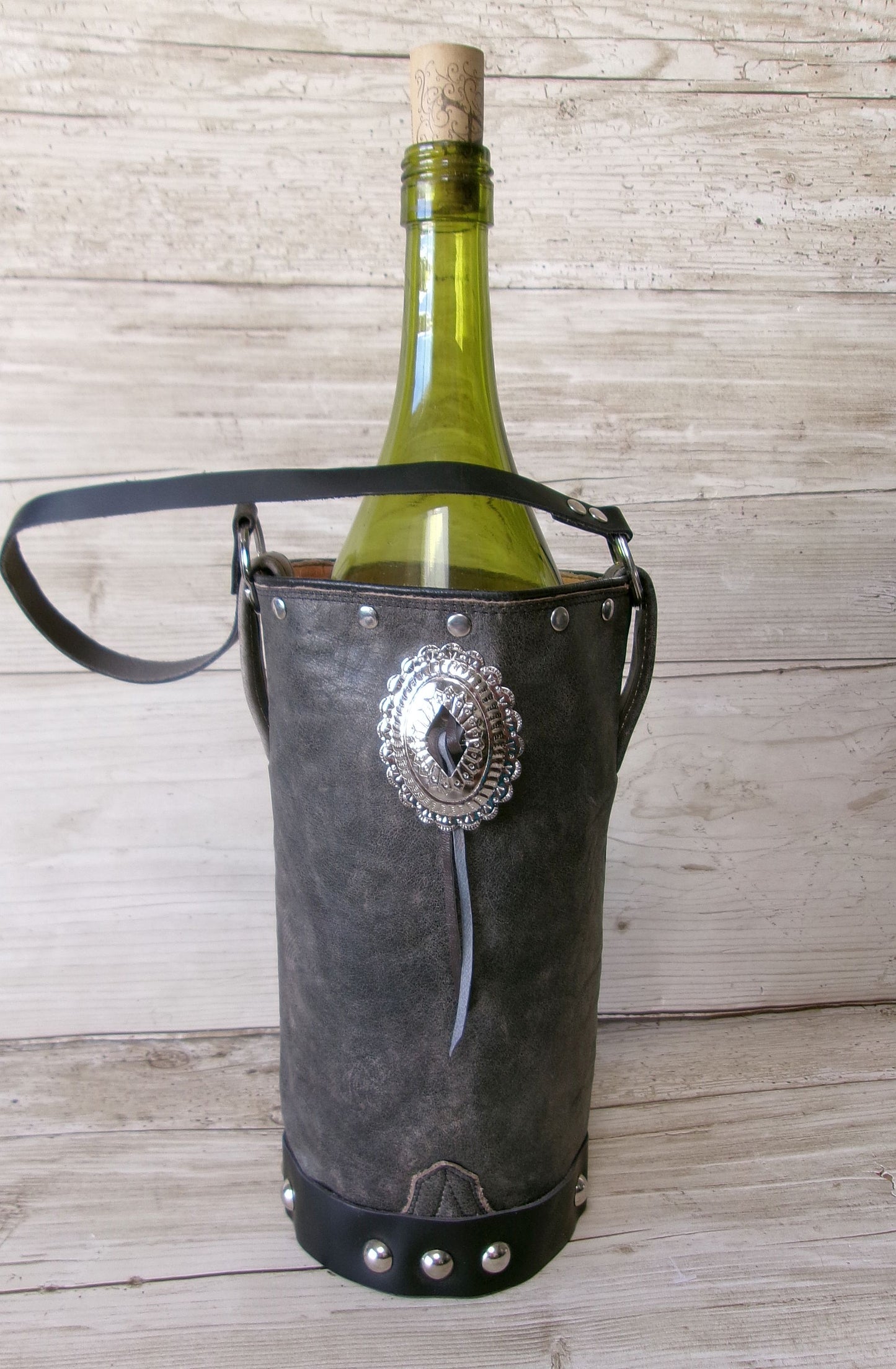 Wine bottle in a decorative leather holder with metal emblem on a wooden background